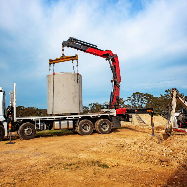 Articulating Boom (Knuckle Boom) Cran Crane truck lowering a concrete septic sewage tank into the ground